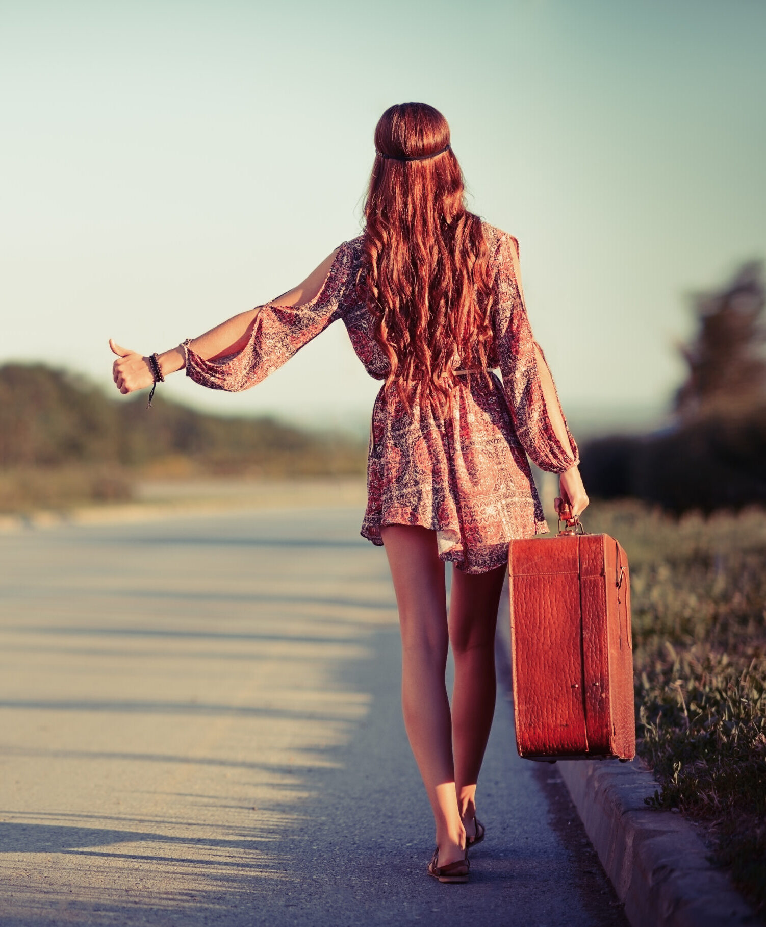 Young hippie woman hitchhiking on a road. Rear view Young hippie woman hitchhiking on the road. Rear view